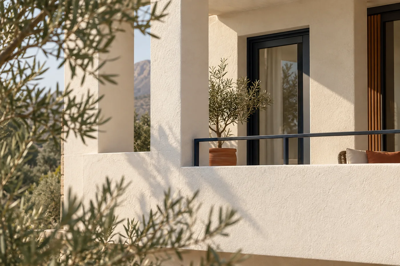 Beyaz sıvalı modern bir binanın balkonu, zeytin dalları ve öğleden sonra ışığı